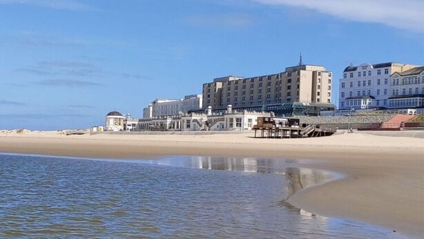 Un hôtel situé en bord de mer, composé de plusieurs bâtiments, avec une plage de sable et une mer calme.
