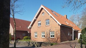Une maison à deux étages, construite en briques, avec un toit recouvert de tuiles rouges, un petit porche à l’avant et une allée pavée.