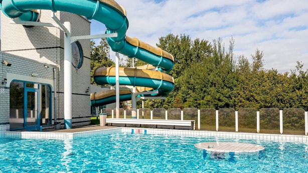 Un parc aquatique doté d’un toboggan aquatique à plusieurs niveaux, d’une piscine et d’un bâtiment à la façade en briques.