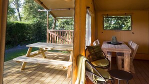 Une terrasse en bois avec des tables et des chaises pour pique-niquer, un espace de repos abrité et une fenêtre donnant sur la verdure.