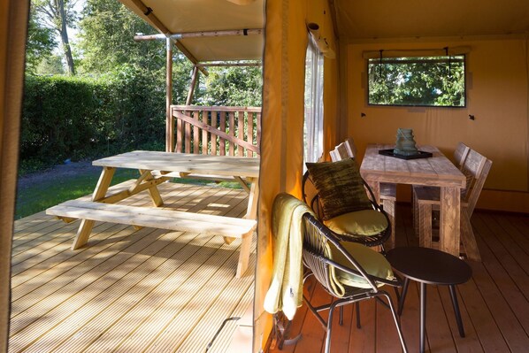 A wooden deck with picnic tables and chairs, a covered seating area, and a window overlooking greenery.