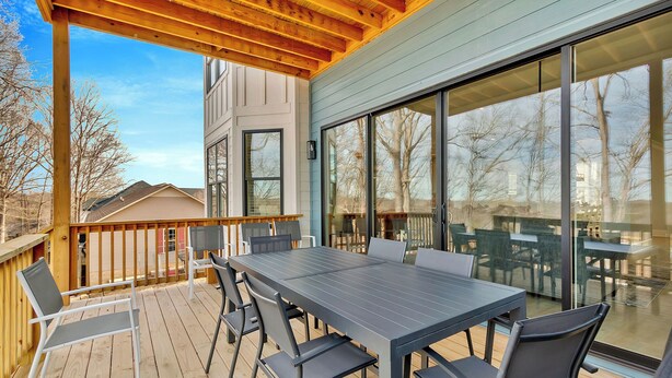 Une terrasse couverte avec une table et des chaises, de grandes fenêtres et une vue sur les environs.
