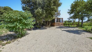 A gravel driveway leading to a rustic wooden cabin with a covered porch, surrounded by lush greenery and trees. - Cozy (sta)caravan in Pernes-les-Fontaines (Pernes-les-Fontaines)