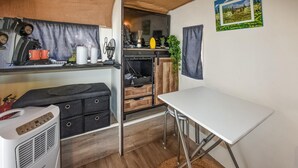 A compact kitchen with a white table, a black cabinet, and a small heater. - Cozy (sta)caravan in Pernes-les-Fontaines (Pernes-les-Fontaines)
