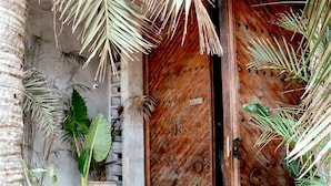 A wooden door with a metal handle, surrounded by tropical plants and a stone wall. - BT Homes - Tankah Beachfront (Tulum)