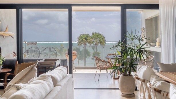 A spacious living area with a large sliding glass door leading to a balcony overlooking the ocean. - BT Homes - Tankah Beachfront (Tulum)