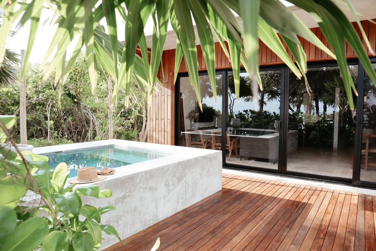 Un espace piscine extérieur moderne, doté d’une terrasse en bois, d’une piscine en béton et d’un patio vitré aménagé avec du mobilier d’extérieur.