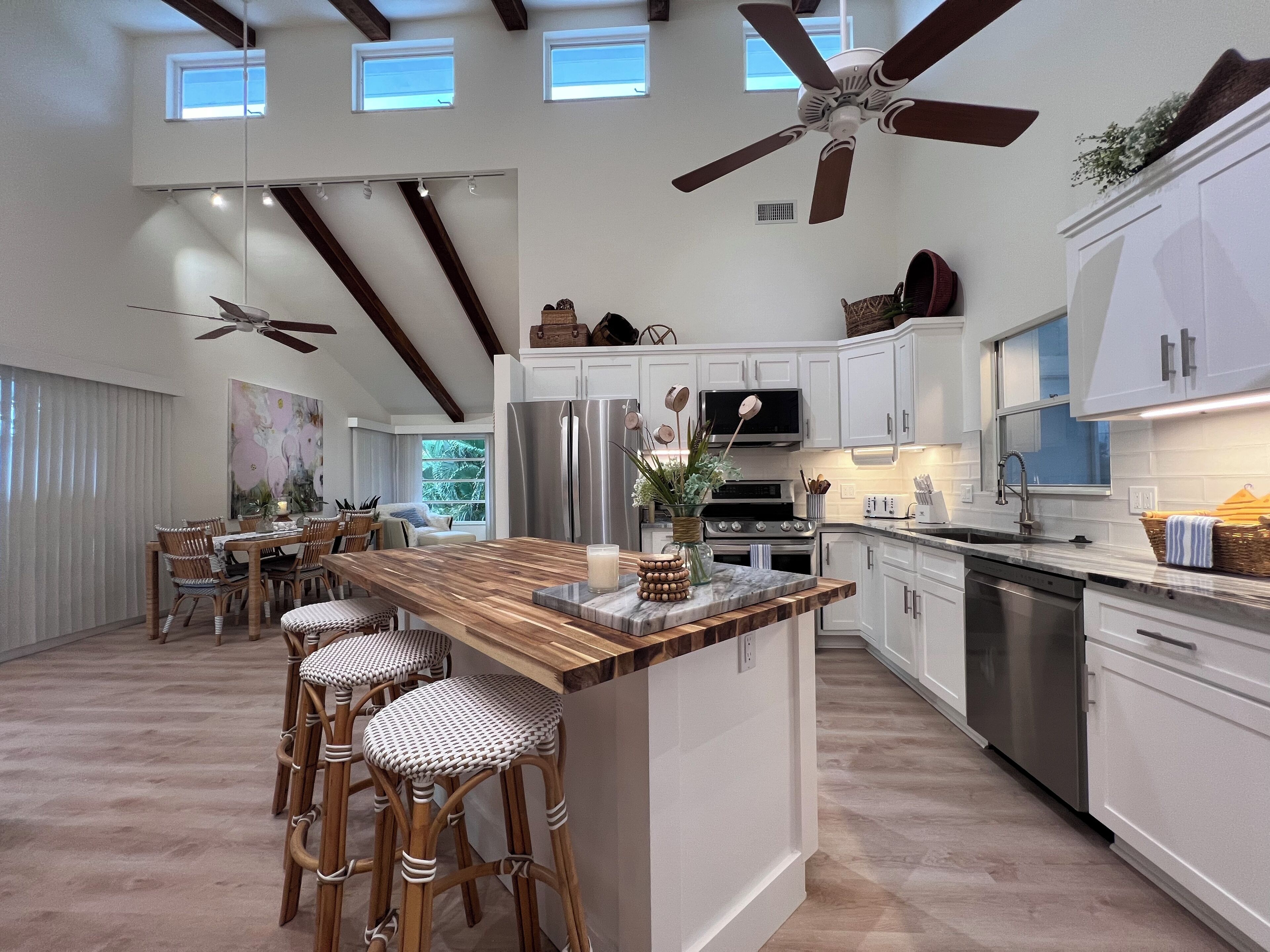 A modern kitchen with a central island, bar stools, and a ceiling fan.