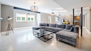 A spacious living room with a sectional sofa, a coffee table, pendant lights, and a large window providing natural light. - Unique Industrial designer studio (Aurora)