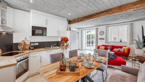 A modern kitchen with white cabinets, a wooden dining table set for four, and a red sofa in the living area. - Cozy apartment in Irrhausen with sauna (Irrhausen)
