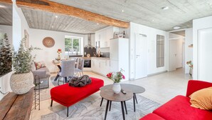 A modern living room with a red sofa, a round coffee table, and a dining area with a kitchen in the background. - Cozy apartment in Irrhausen with sauna (Irrhausen)