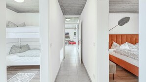 A narrow hallway with bunk beds on the left and a sofa bed on the right, leading to a dining area with a red chair and table. - Cozy apartment in Irrhausen with sauna (Irrhausen)