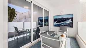 Un balcón con puerta de vidrio, muebles blancos y un cuadro grande con un paisaje.