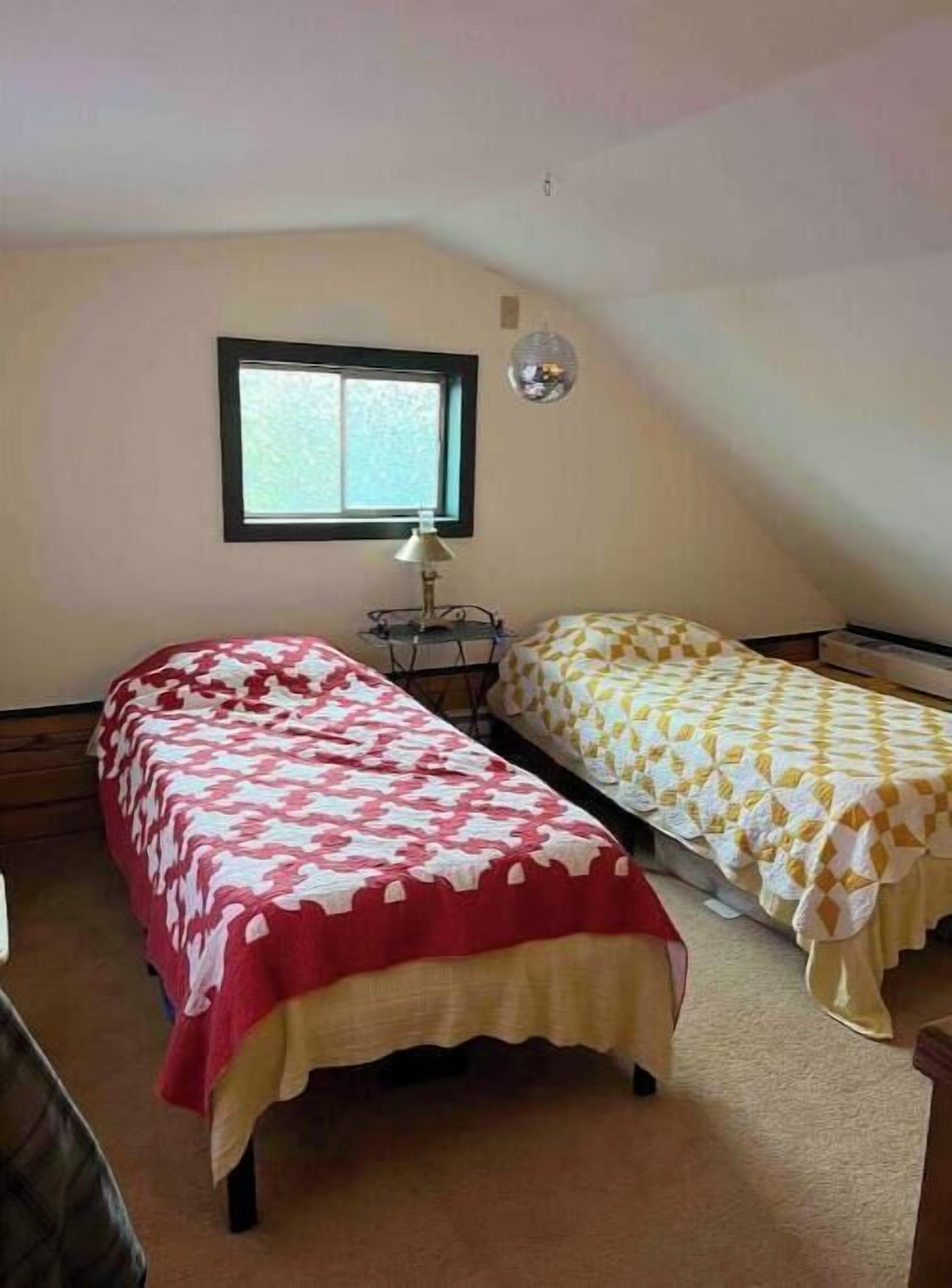 A small, cozy room with two single beds, a window, and a hanging lamp.