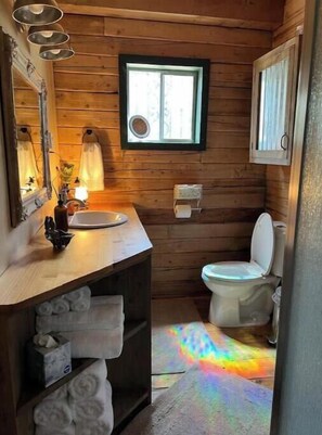A wooden cabin bathroom with a wooden vanity, a sink, a toilet, and a window.