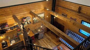 A high-ceilinged wooden interior with a bar area, a staircase, and a 'Welcome' sign.
