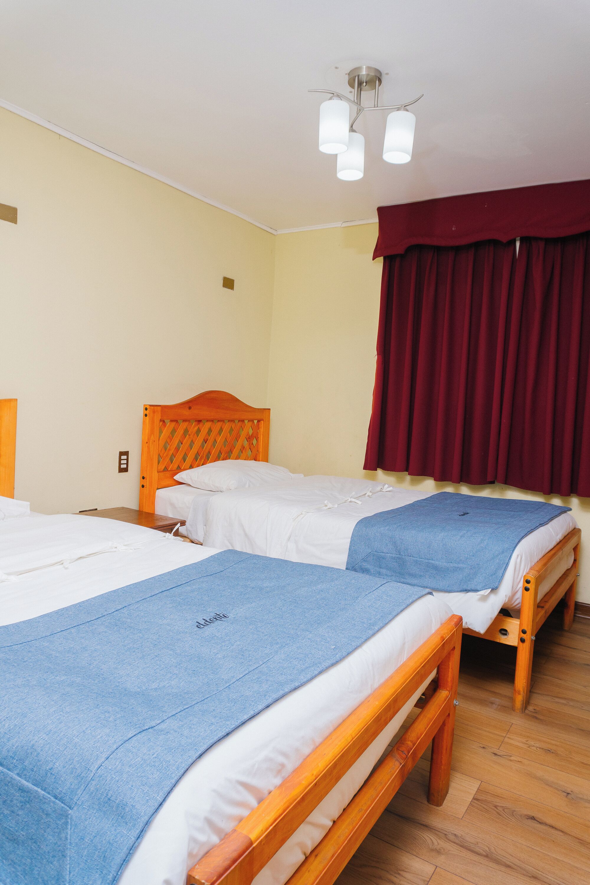 Una habitación con dos camas de madera, una cortina roja y una lámpara en el techo.