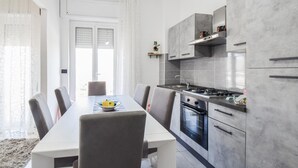 Una cocina moderna con armarios grises, una campana extractora de acero inoxidable y una zona de comedor con una mesa blanca y sillas grises.