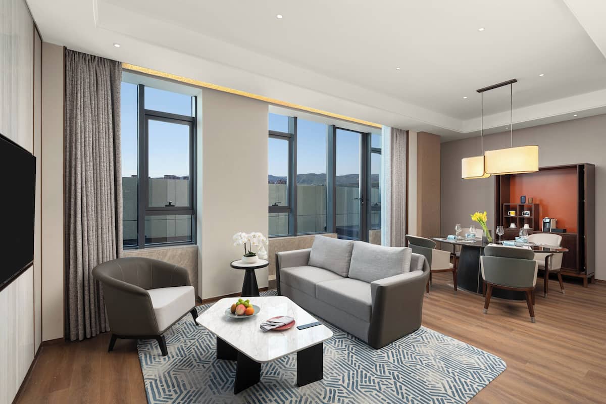 Una habitación de hotel moderna con sofá, sillones, una mesa de comedor y televisión.