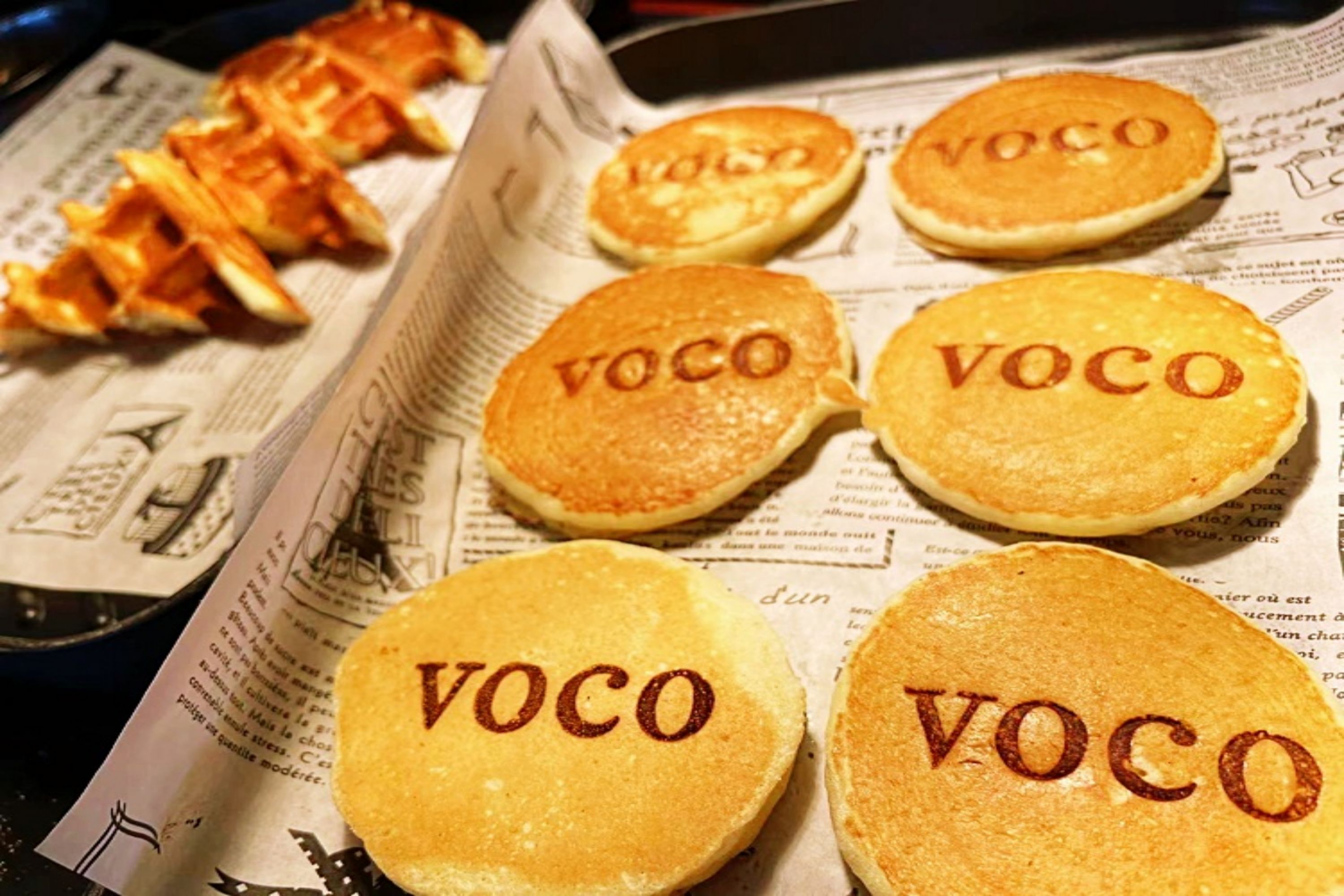 Una bandeja de panqueques con la palabra 'VOCO' impresa, sobre un periódico.