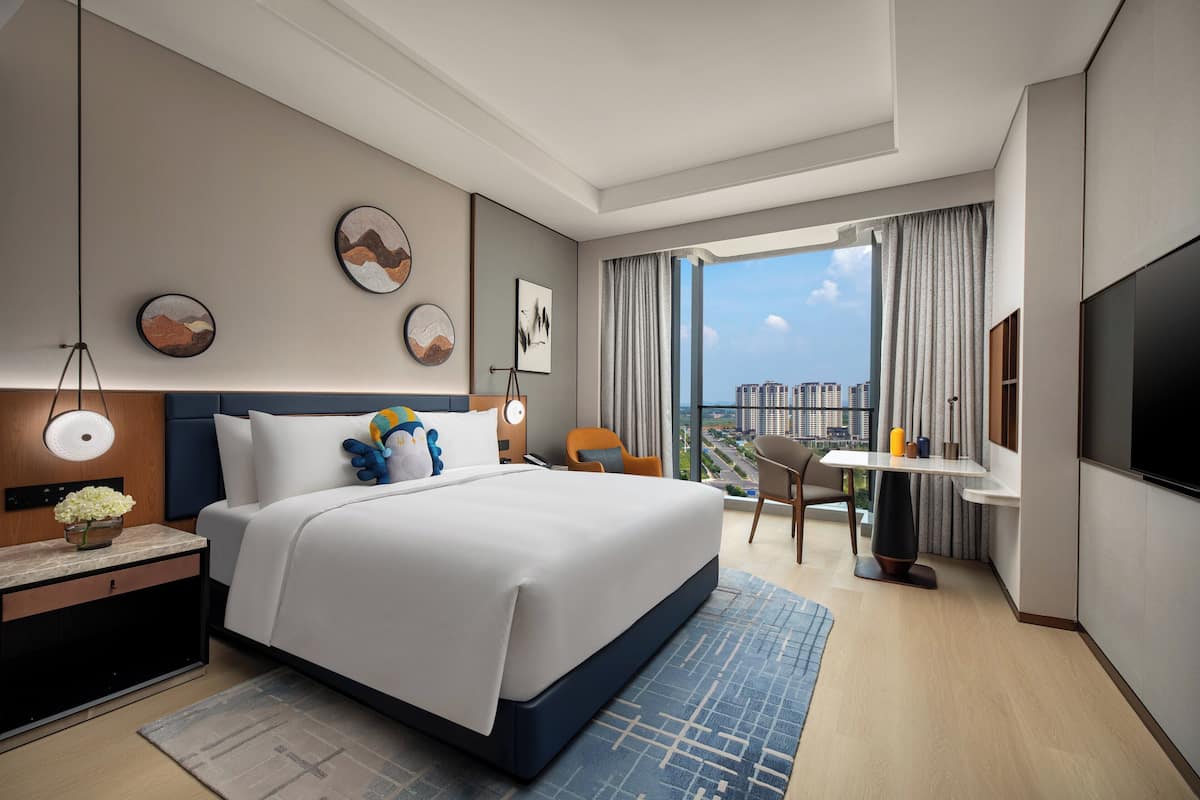 Habitación de hotel moderna con una cama grande, un escritorio, una silla, un televisor y vistas a la ciudad.