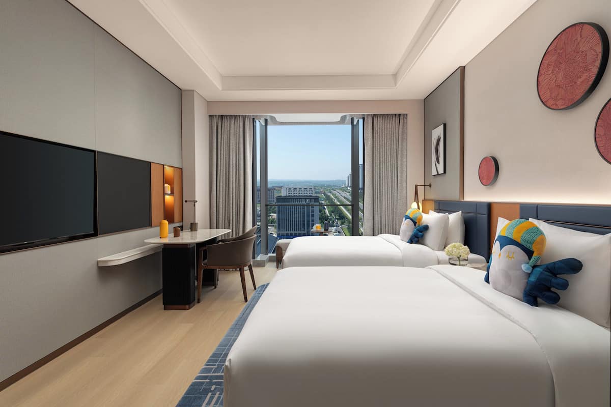 Habitación de hotel con dos camas, un escritorio y vistas a la ciudad.