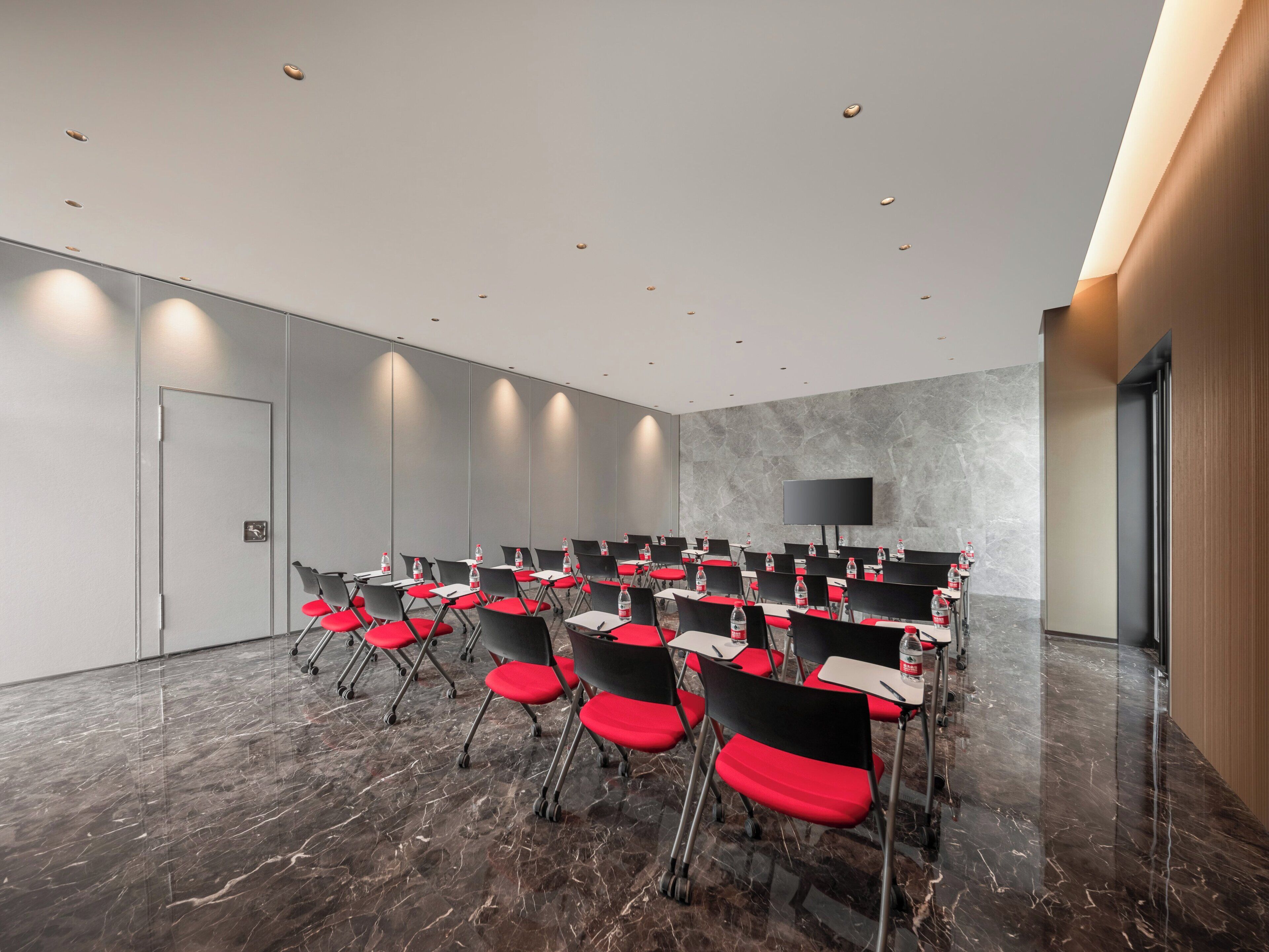 A conference room with rows of chairs, a large flat-screen TV, and a marble floor.