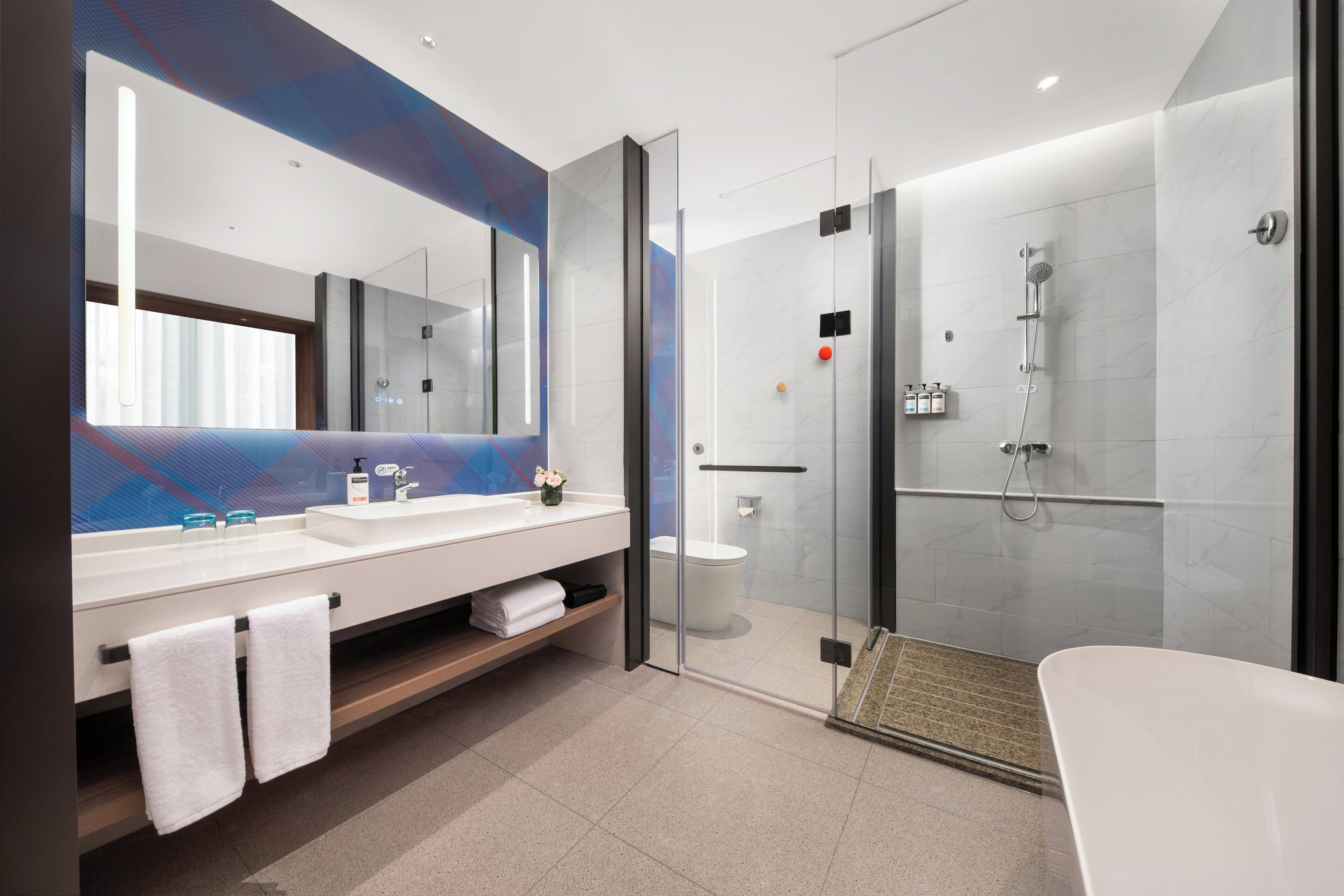 Un baño moderno con ducha envuelta en cristal, una bañera blanca y un espejo grande sobre el lavabo.