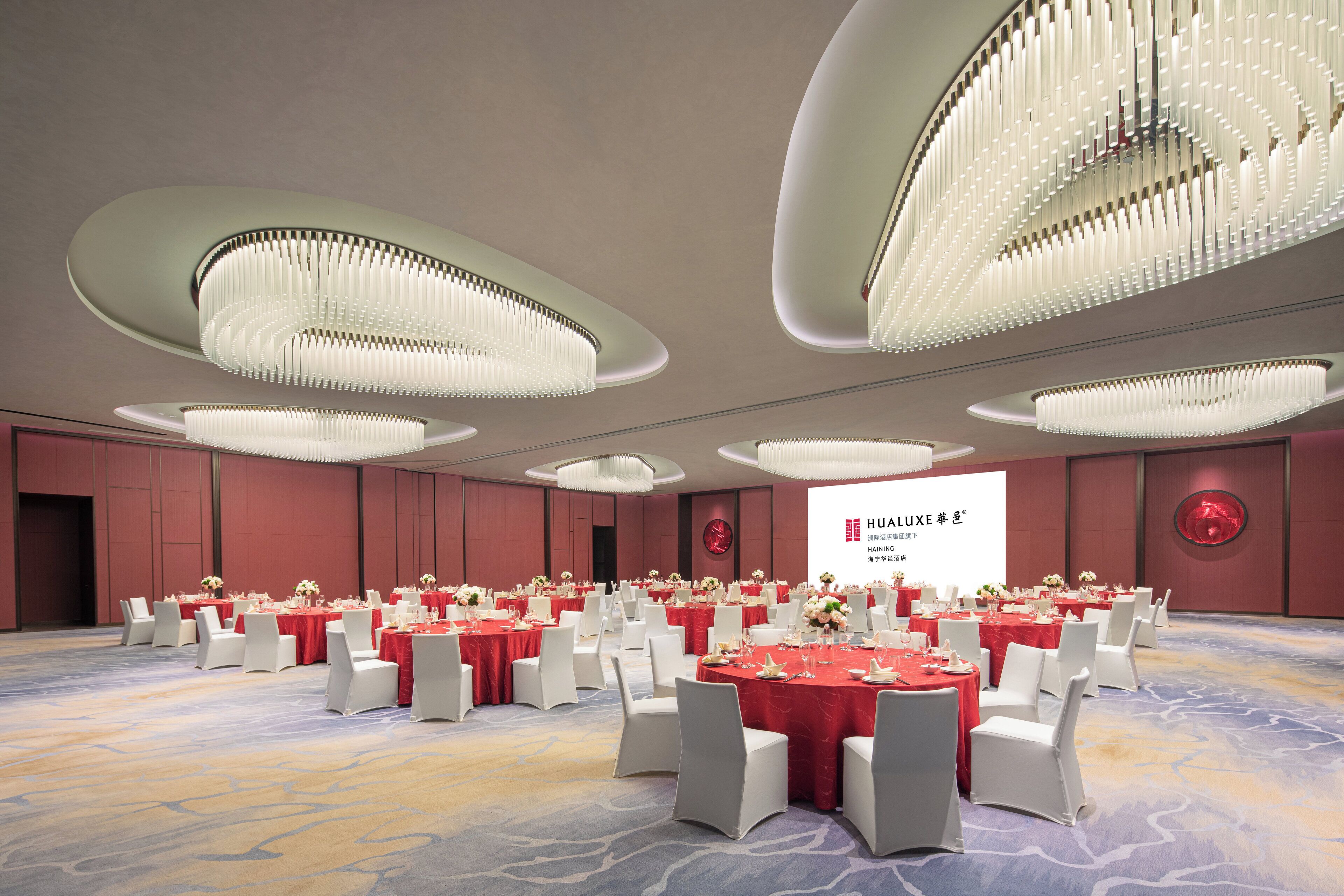 A conference room with multiple tables set for a meeting, featuring a large screen and elegant chandeliers.