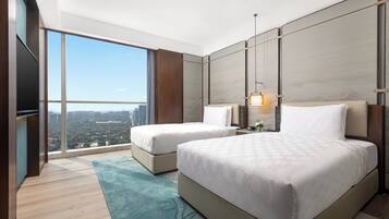 A modern hotel room with a large window, two beds, a flat-screen TV, and a city view.