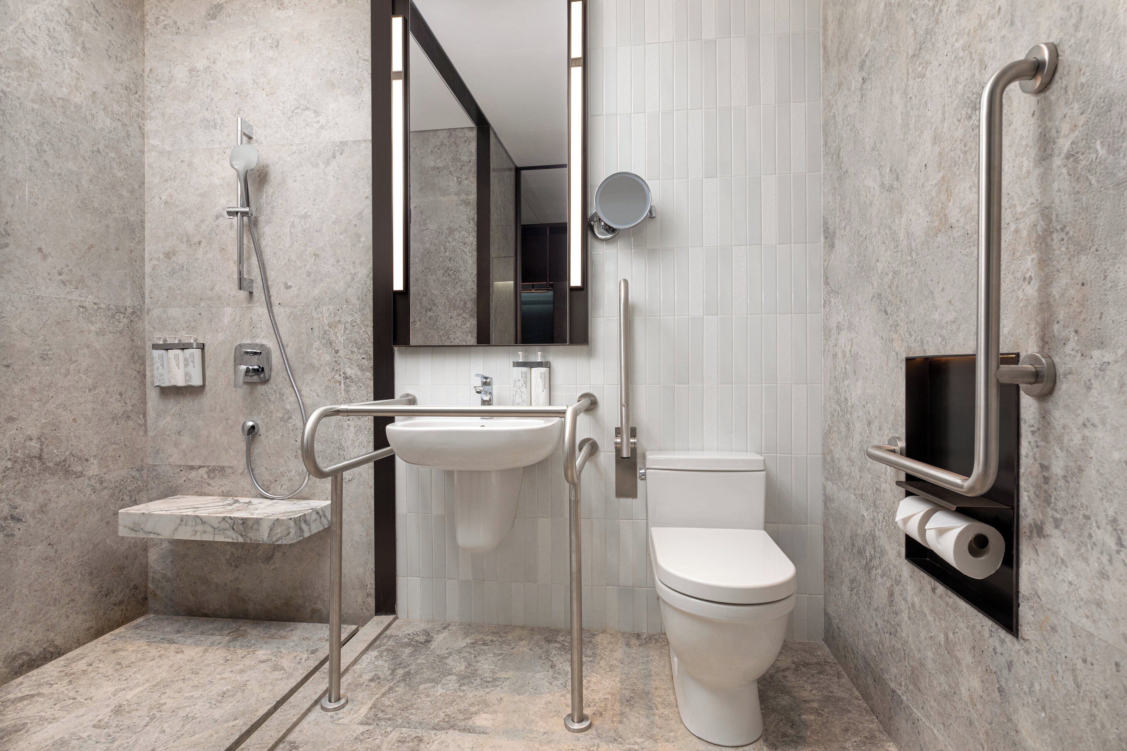 Un baño moderno con lavamanos de mármol, inodoro, ducha y barra de apoyo.