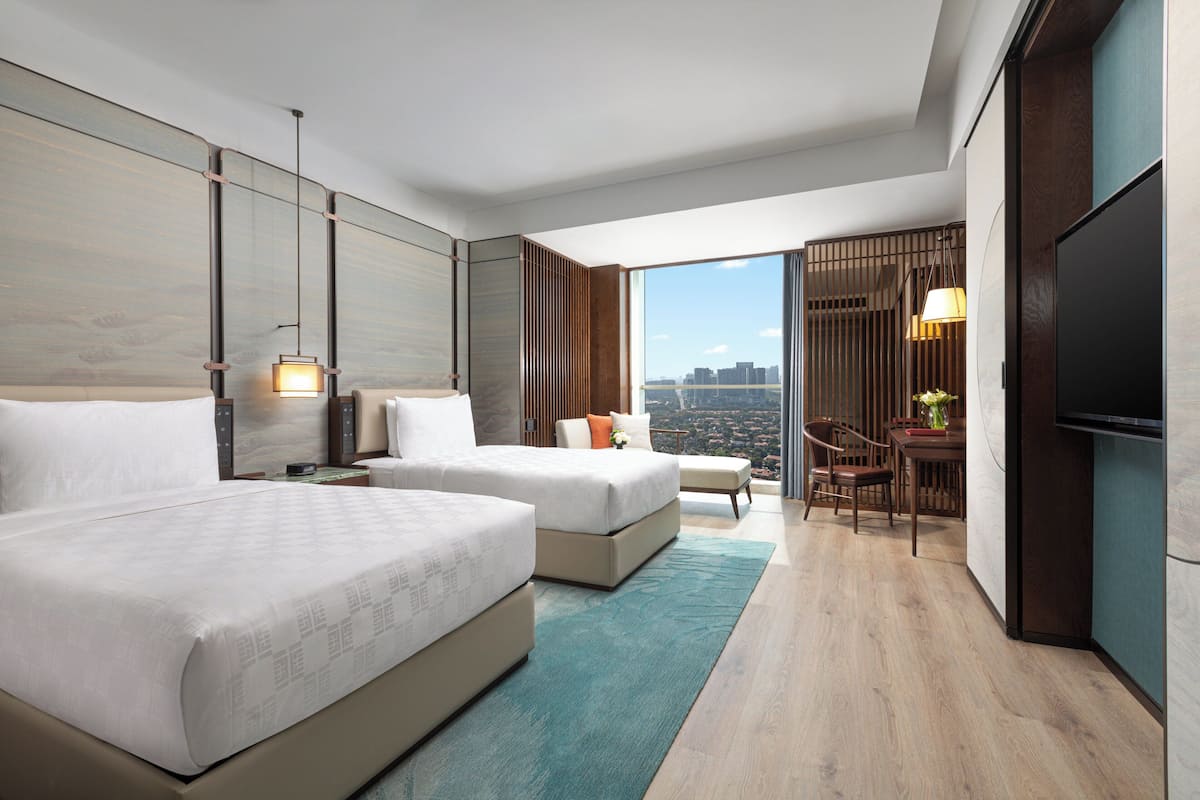 A modern hotel room with two beds, a desk, a chair, and a large TV.