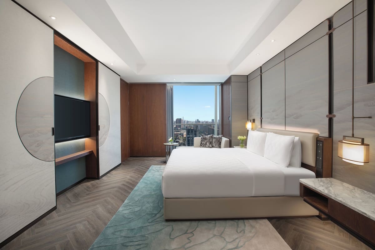 A modern hotel room with a large bed, a TV, and a city view.