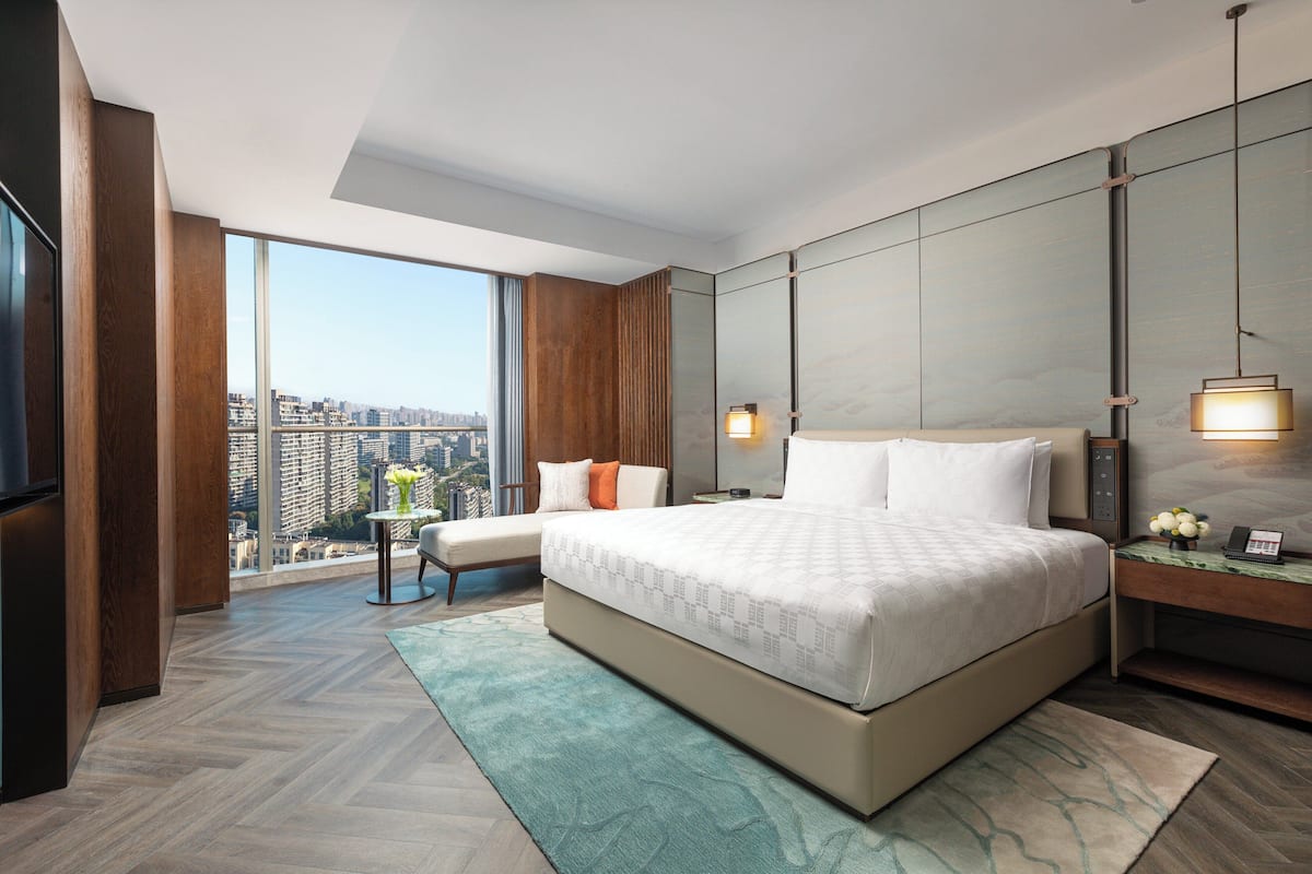 A modern hotel room with a large bed, a seating area, a TV, and a city view.