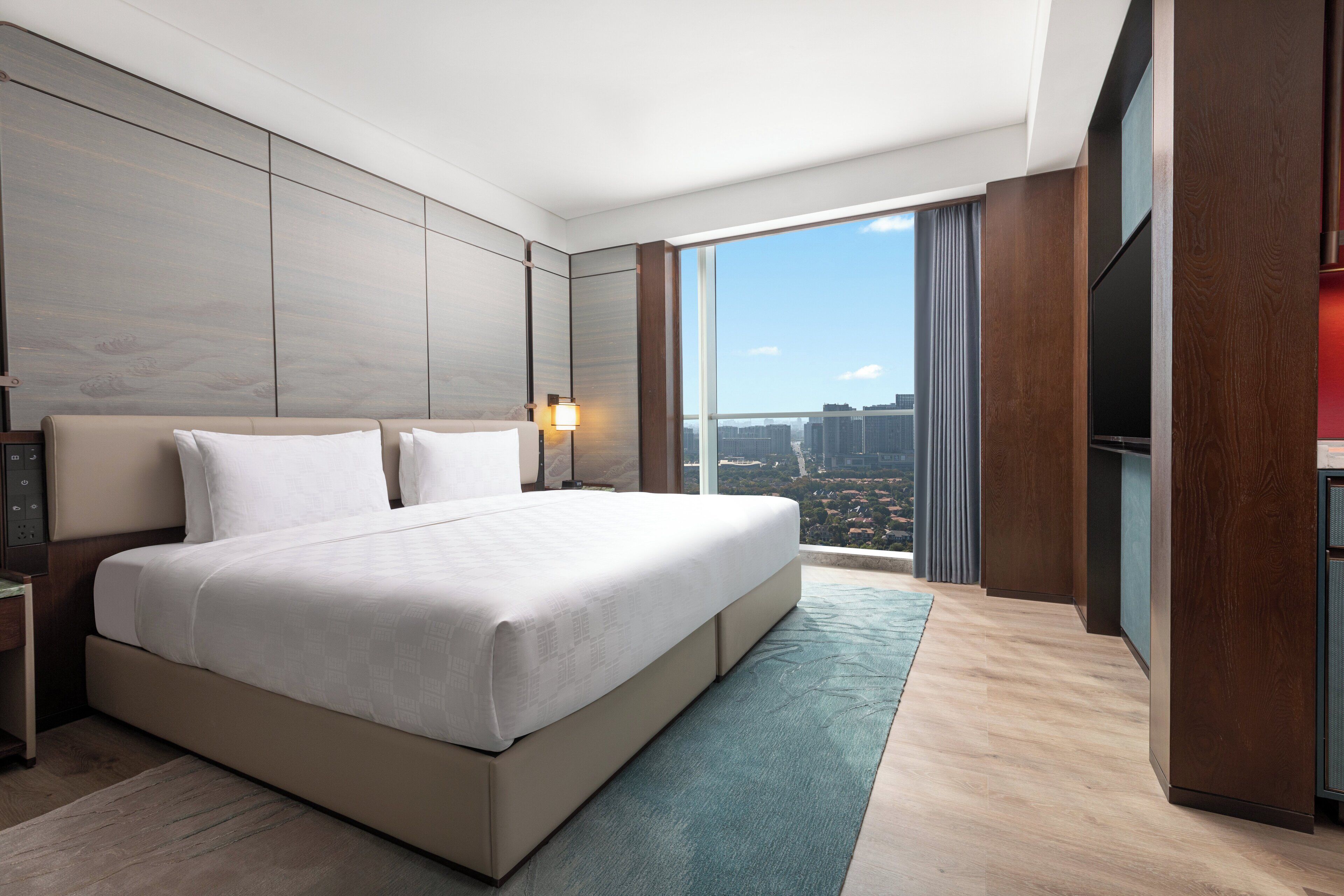 Ein modernes Hotelzimmer mit einem großen Bett, Blick auf die Stadt und einem Flachbildfernseher.