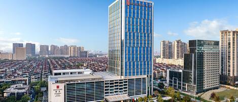 A modern high-rise building with a prominent Hualux hotel sign, surrounded by a well-maintained urban area with clear roads and greenery.