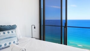 A hotel room with a bed, a view of the ocean, and a large window.