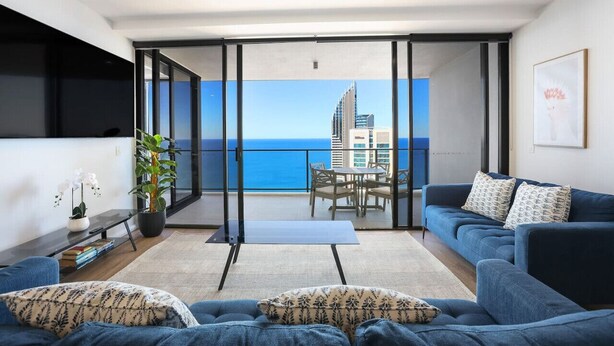 A modern living room with a balcony, a dining area, and a view of a city skyline.