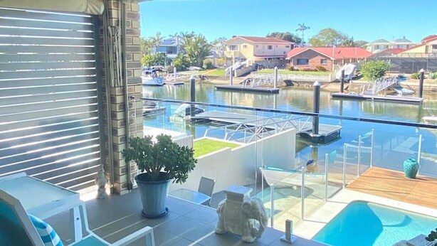 A balcony with a pool, lounge chairs, and a view of a marina with boats and houses.