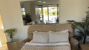 A neatly made bed with striped bedding and tassels, a large mirror above it, and a view of the outdoors through a sliding door.
