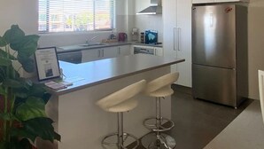 A modern kitchen with white cabinets, a stainless steel refrigerator, a bar stool area, and a ceiling fan.