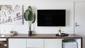 A modern hotel room with a wooden desk, a flat-screen TV, a potted plant, and a minibar. - NEW Central Surfers Studio Apartment. (Surfers Paradise)
