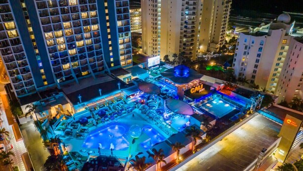 A hotel with a rooftop pool area, multiple balconies, and a well-lit urban setting. - NEW Central Surfers Studio Apartment. (Surfers Paradise)