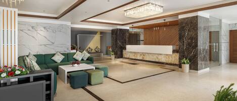 A spacious lobby with a green sofa, a coffee table, and a seating area with ottomans. There is a reception desk with a marble countertop and a large chandelier above.