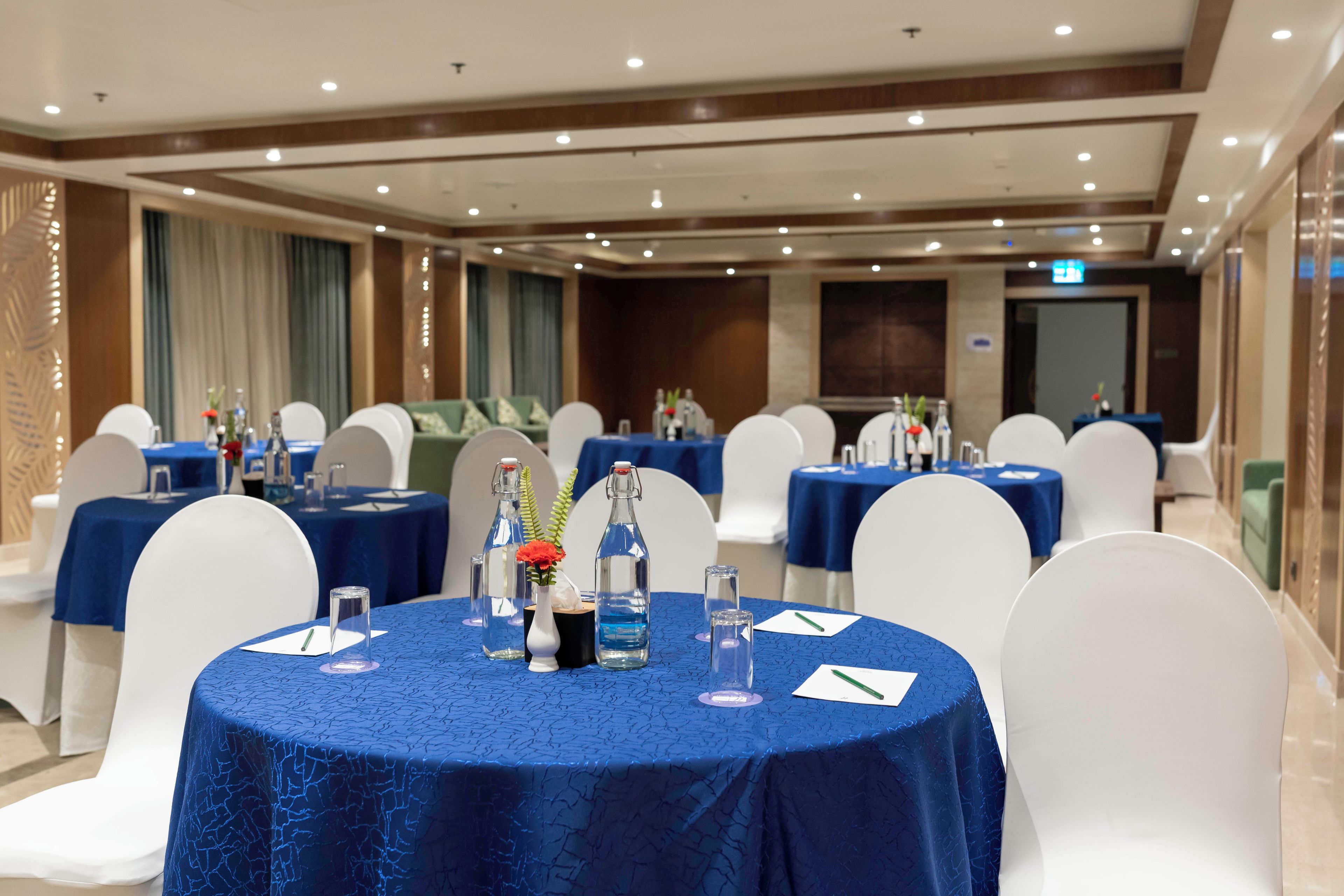 Un salón de conferencias con mesas redondas, sillas blancas y manteles azules.
