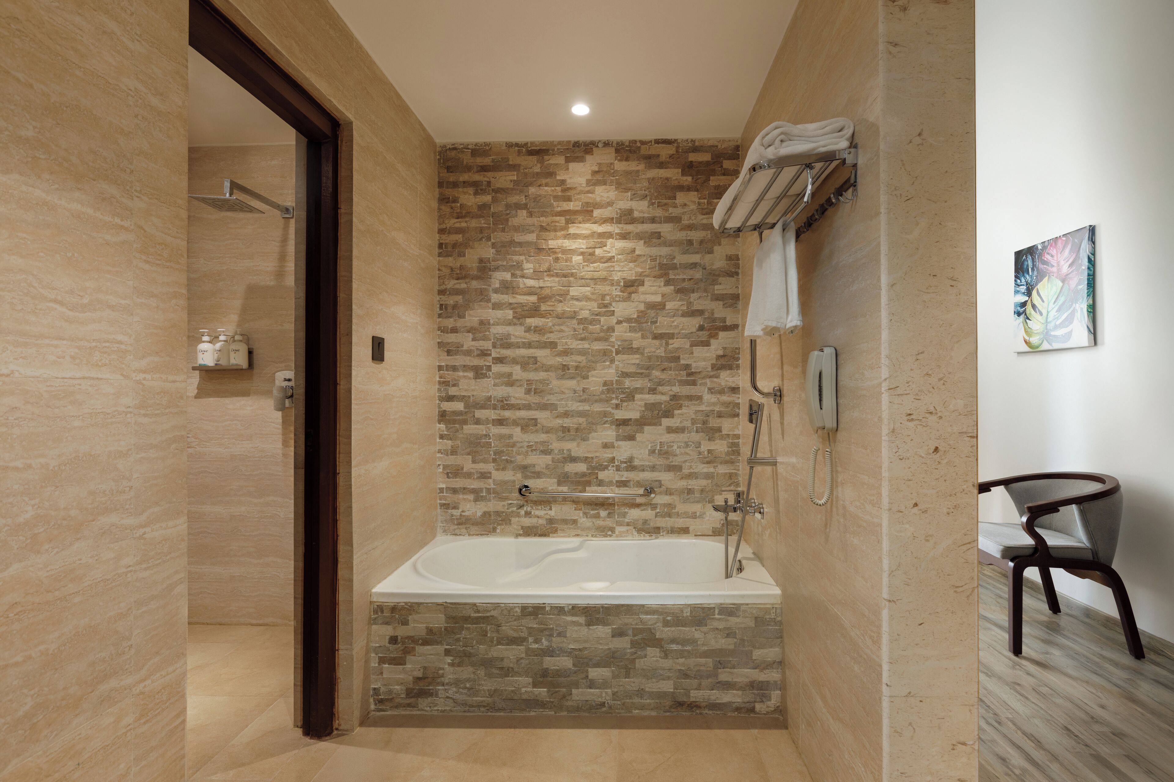A modern bathroom with a stone mosaic wall, a freestanding bathtub, a towel rack, and a chair.