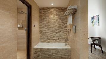 A modern bathroom with a stone mosaic wall, a freestanding bathtub, a towel rack, and a chair.