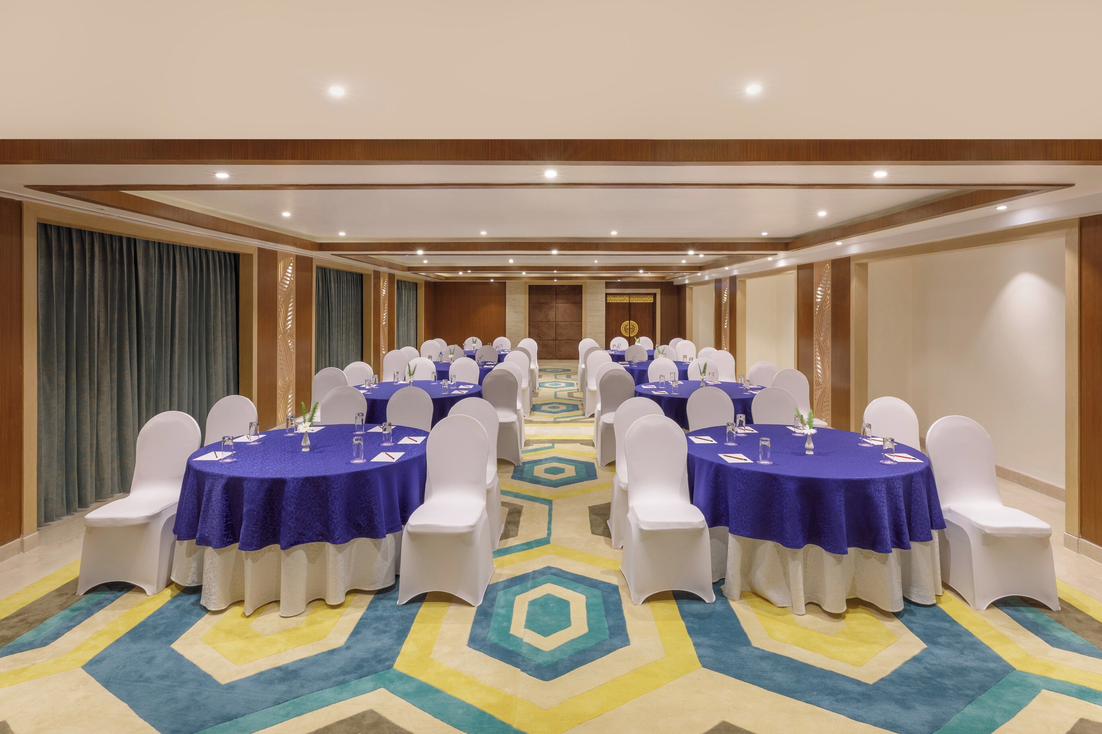 A conference room with multiple tables, white chairs, and a patterned carpet.