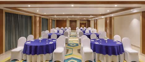 A conference room with multiple tables, white chairs, and a patterned carpet.
