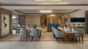 A modern dining area with a chandelier, marble walls, and a mix of seating styles including chairs and a wicker chair. - Holiday Inn Resort Kathmandu Budhanilkantha by IHG (Burhanilkantha)